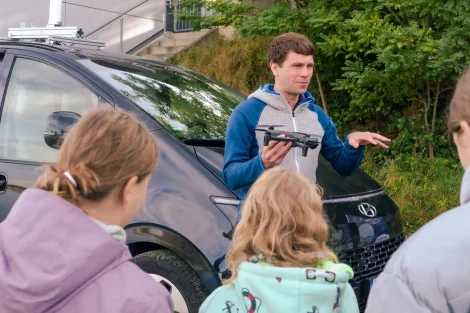 adulto com um drone ambiental na mão com posição explicativa junto a crianças.